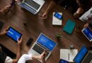 Overhead view of a diverse team discussing around a wooden table, using technology.