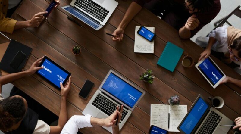 Overhead view of a diverse team discussing around a wooden table, using technology.