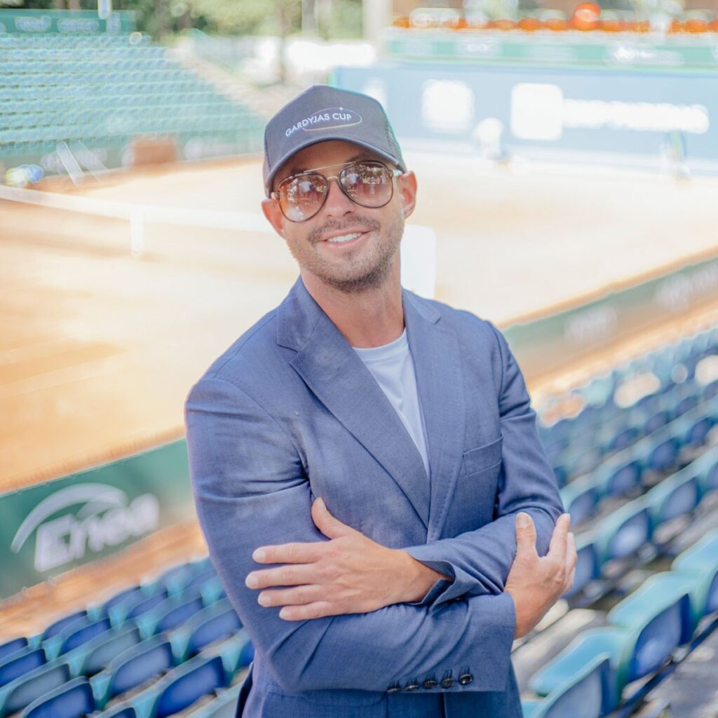 Grzegorz Gardyjas, GLTA Director of Marketing, photographed in a professional headshot, with the background of a clay court tennis venue in Poland.